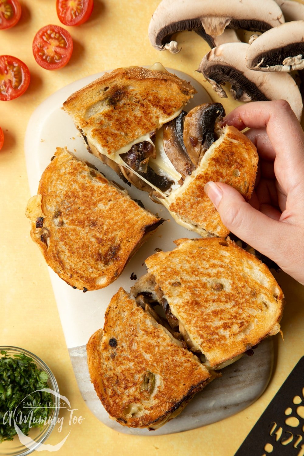 Two Jarlsberg cheese and mushroom toasties are on a serving board, one is being pulled apart so the cheese and mushrooms stretch out between them.
