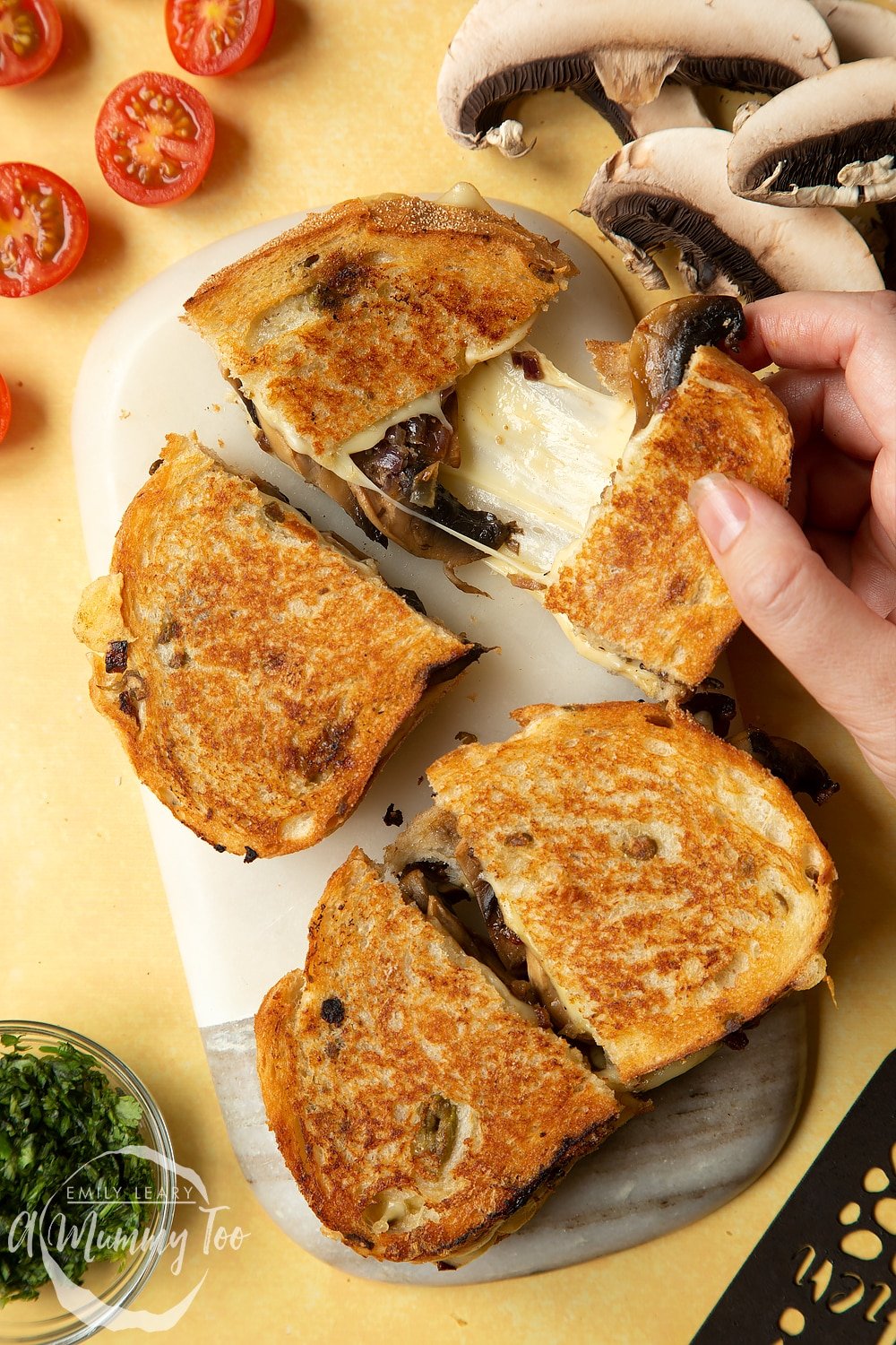 Two Jarlsberg cheese and mushroom toasties are on a serving board, one is being pulled apart so the cheese stretches out between them.