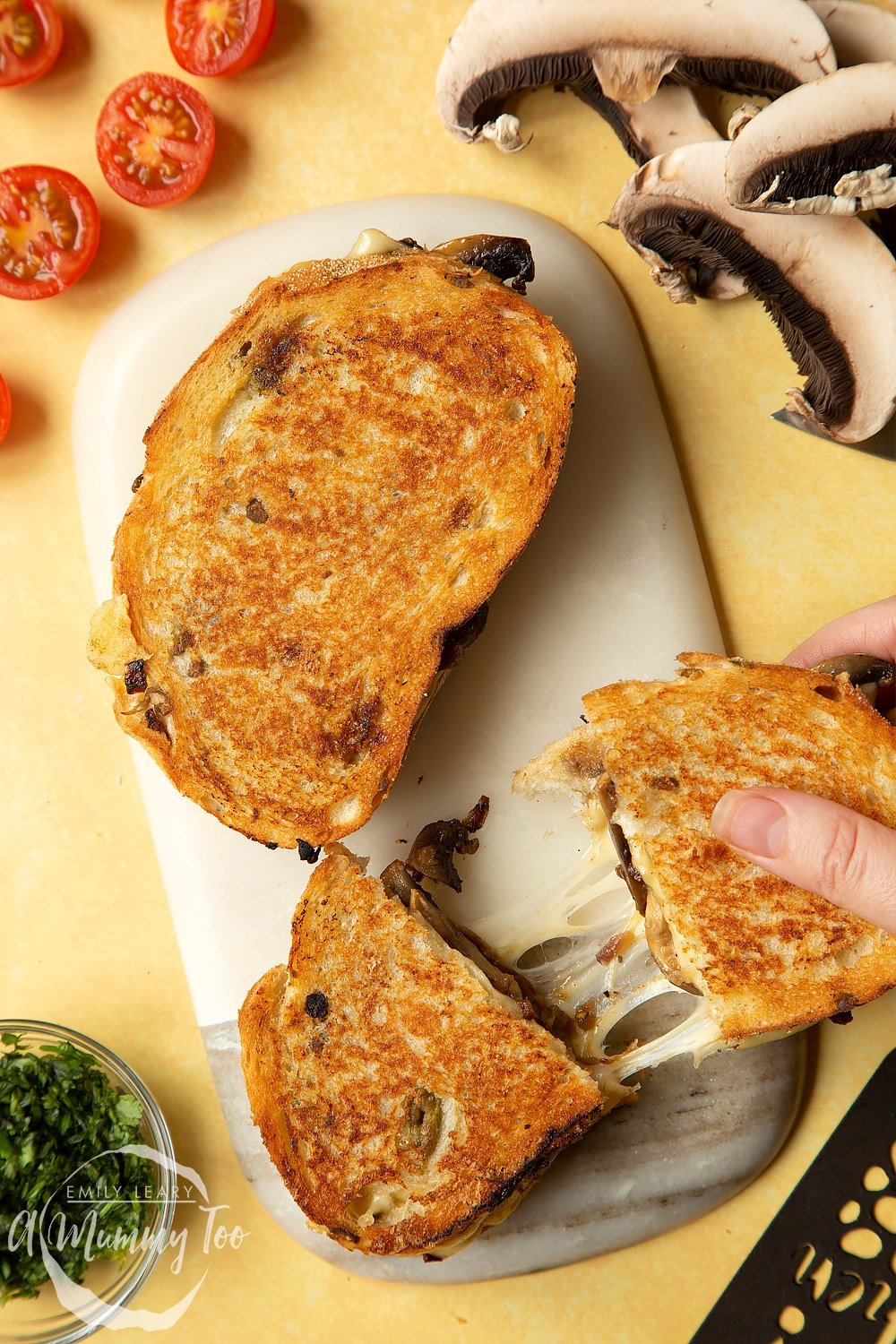 Two Jarlsberg cheese and mushroom toasties are on a serving board, one is being pulled apart so a little bit of cheese stretches out between them.