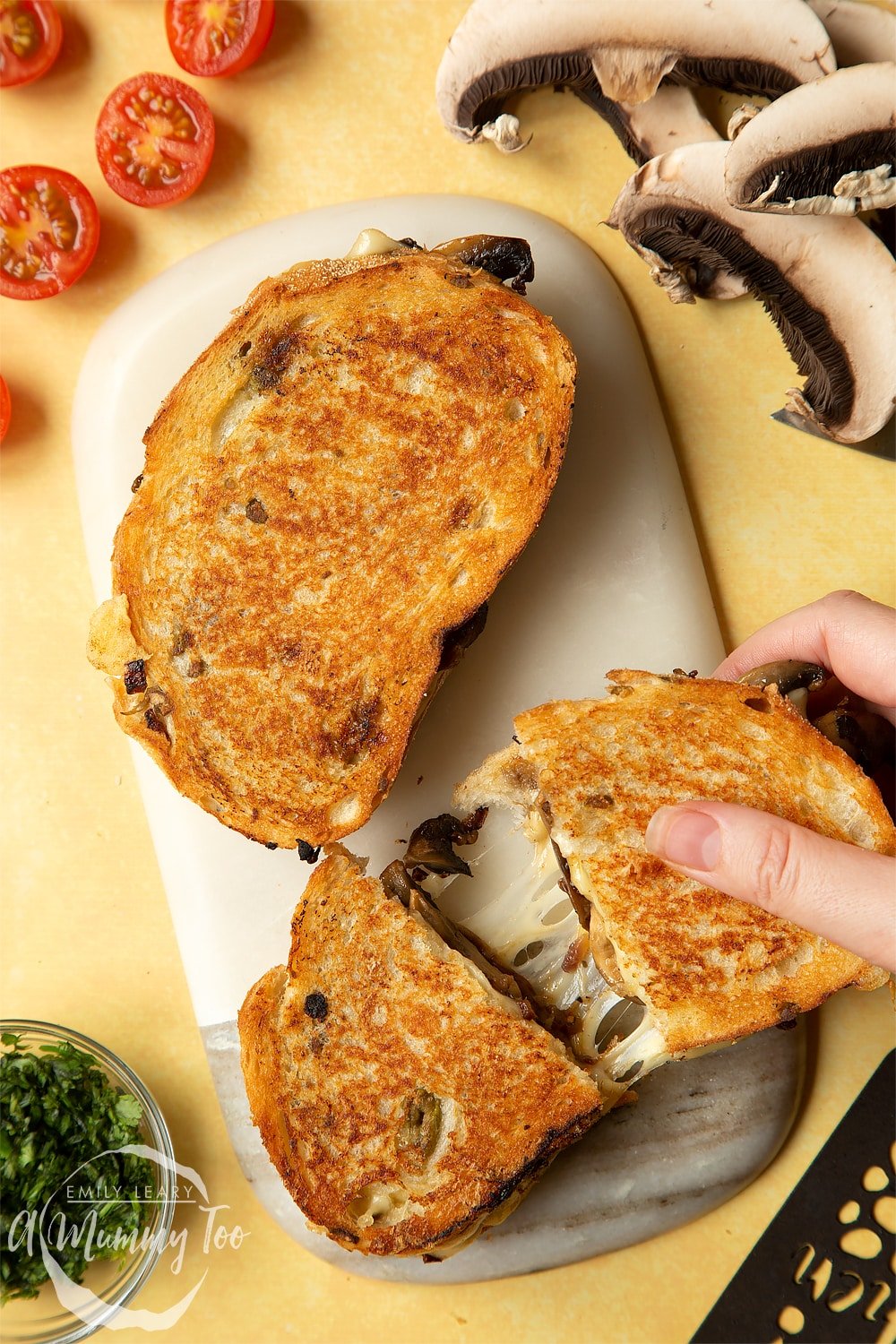 Two Jarlsberg cheese and mushroom toasties are on a serving board, one is being pulled apart so the cheese stretches out between them.