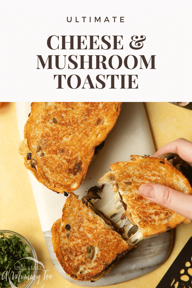 Two Jarlsberg cheese and mushroom toasties are on a serving board, one is being pulled apart very wide, the cheese is stretching between them almost to the point of breaking.