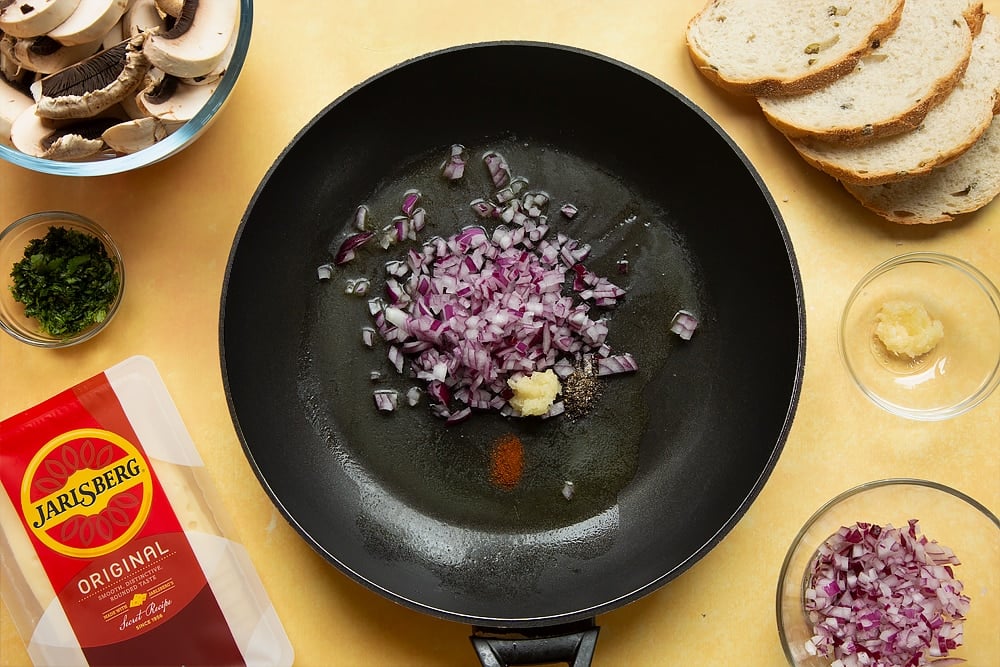 A frying pan with butter melted in it along with uncooked garlic, onions, cayenne and black pepper.