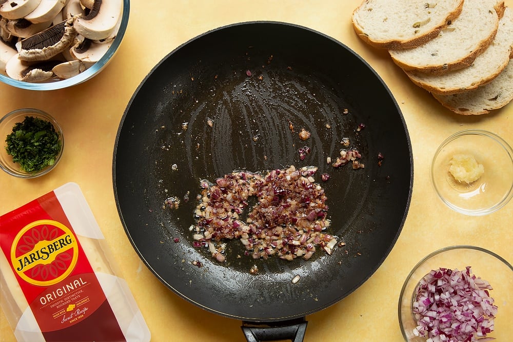 A frying pan with cooked garlic, onions, cayenne and black pepper in it.