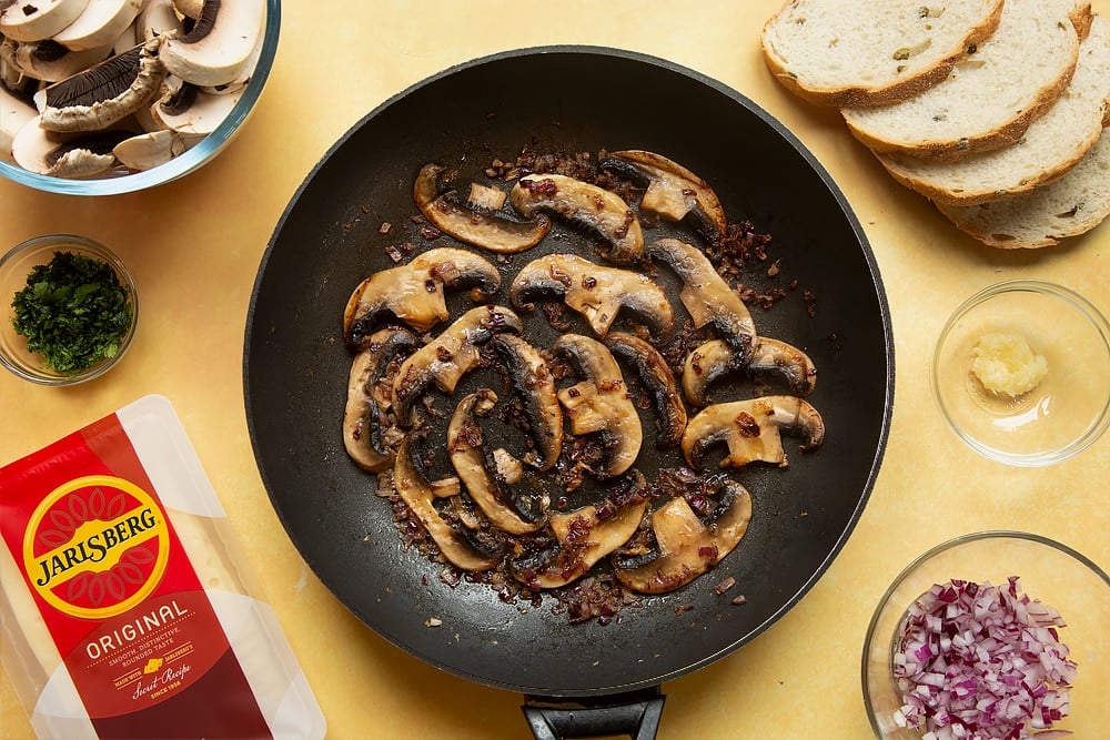 A frying pan with cooked garlic, onions, cayenne and black pepper in along with cooked mushrooms.