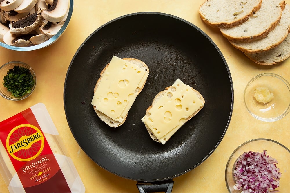 A frying pan with two slices of bread side by side and Jarlsberg cheese on top of both.