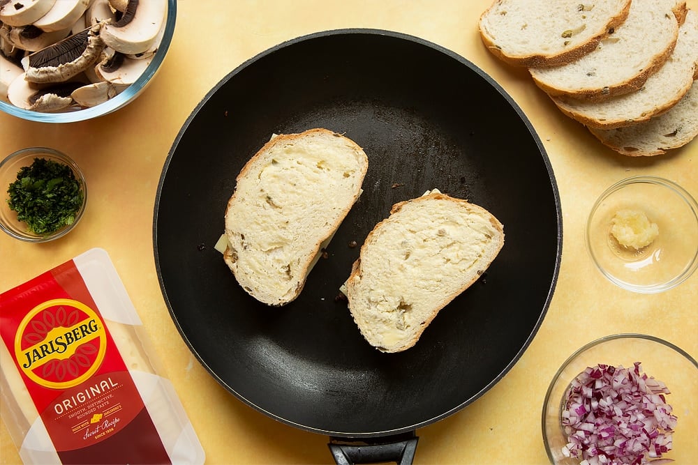 A frying pan with two uncooked but fully constructed toasties in it.