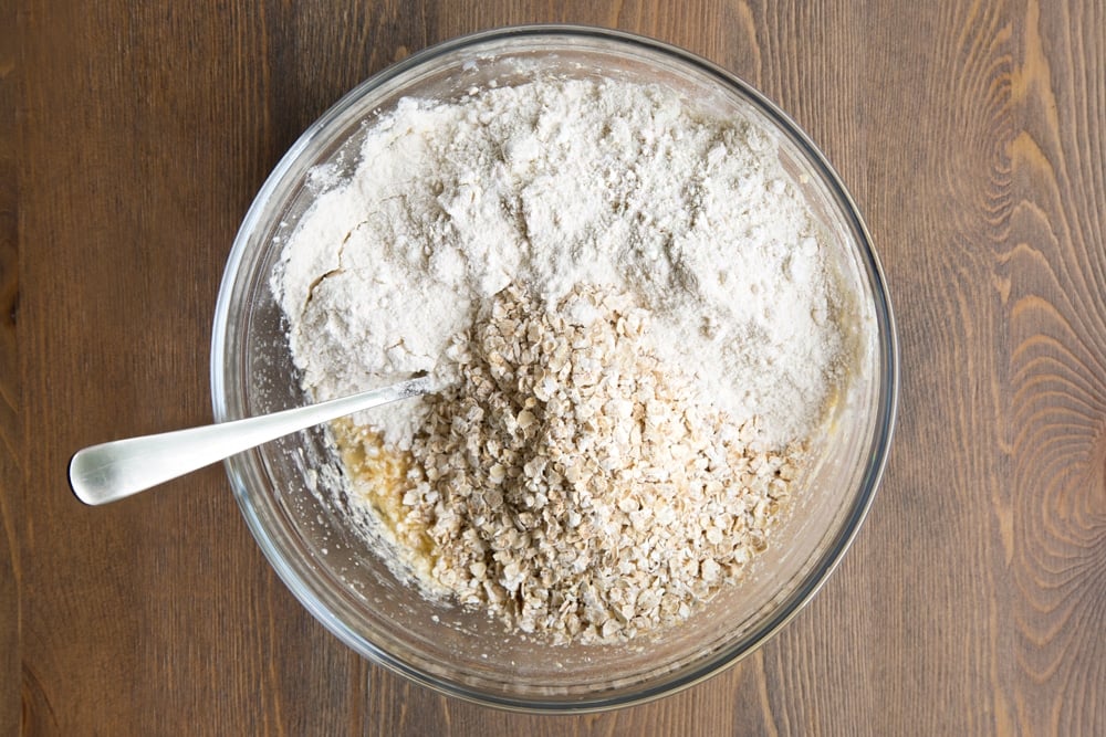 Butter and sugar, milk, egg replacement powder and vanilla creamed together in a bowl, with flour and oats on top.