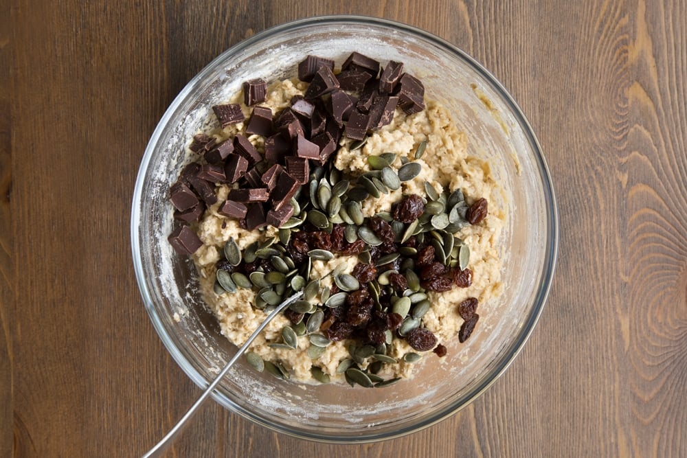 Vegan oat cookie dough in a bowl with chocolate, seeds and raisins on top.