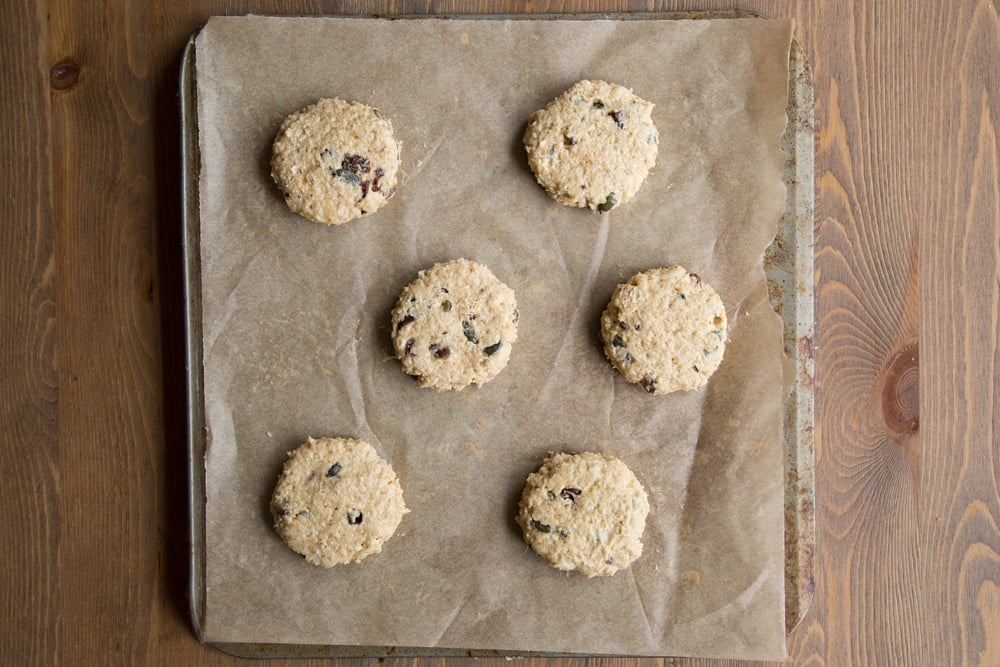 Discs of vegan oat cookie dough on a tray lined with baking paper.