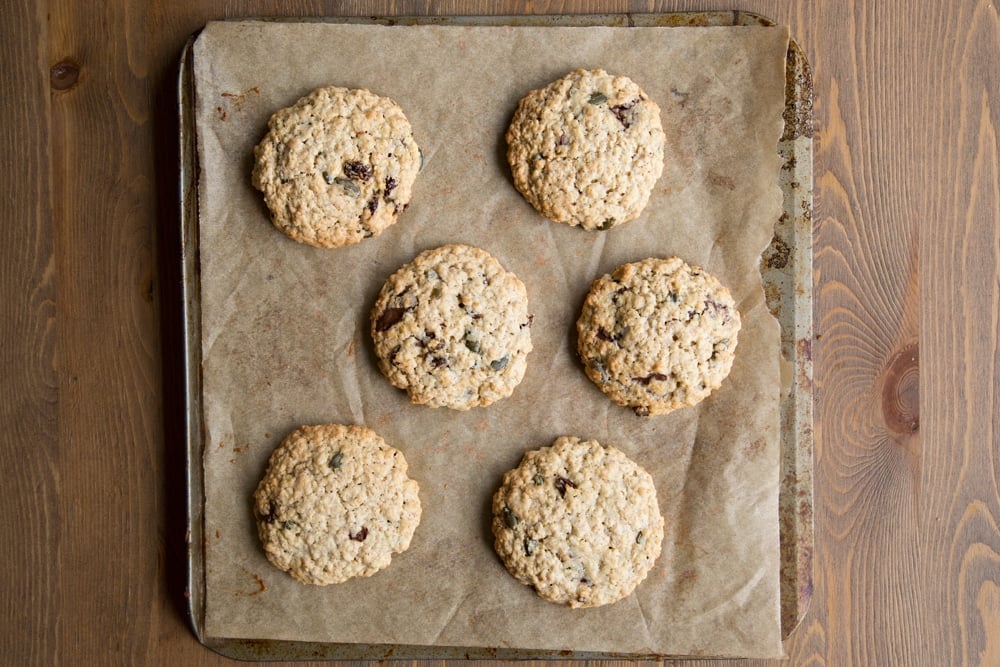 Freshly baked vegan oat cookies on a baking tray lined with baking paper.