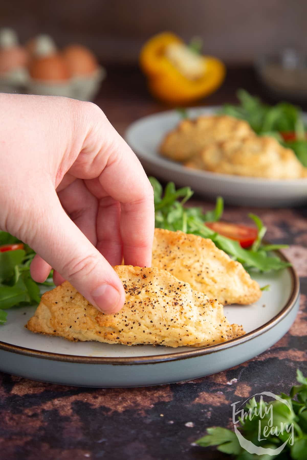 Hand reaching in to grab one of the finished mini cornish pasties sitting on a decorative plate.