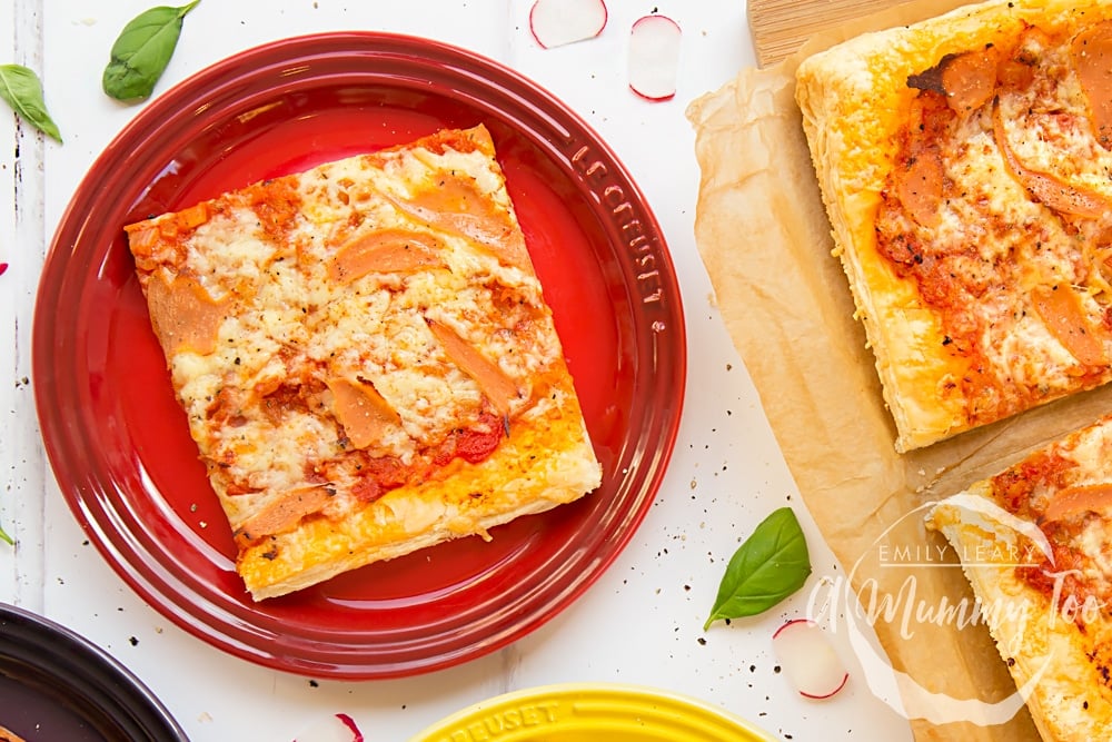 Overhead shot of Pizza style puff pastry slice served on colorful plates with a mummy too logo in the lower-right corner