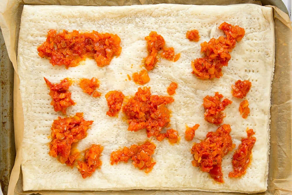 Overhead shot of puff pastry with dollops of tomato sauce on a baking tray lined with parchment paper