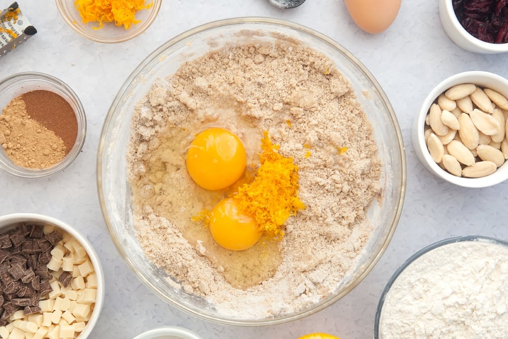 Overhead shot of dough mix, orange zest and eggs in a large clear bowl