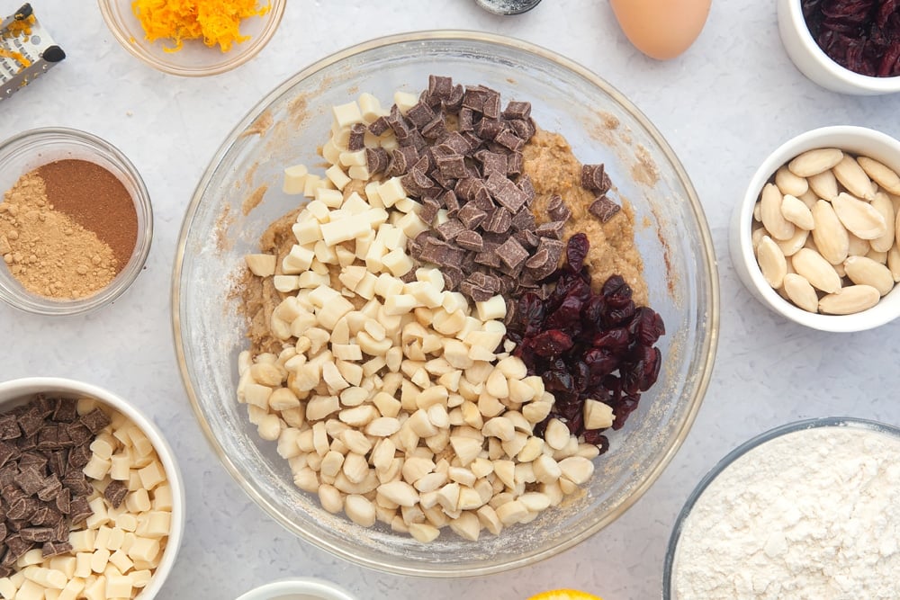 Overhead shot of dough mix, almonds, cranberries and chocolate chips in a large clear bowl