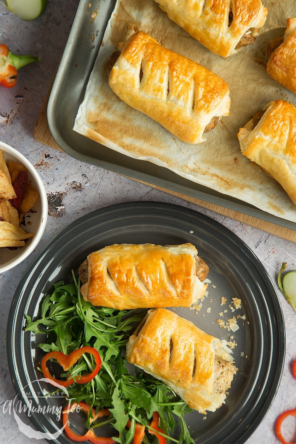 Two vegetarian sausage rolls on a plate with salad and pastry crumbs.