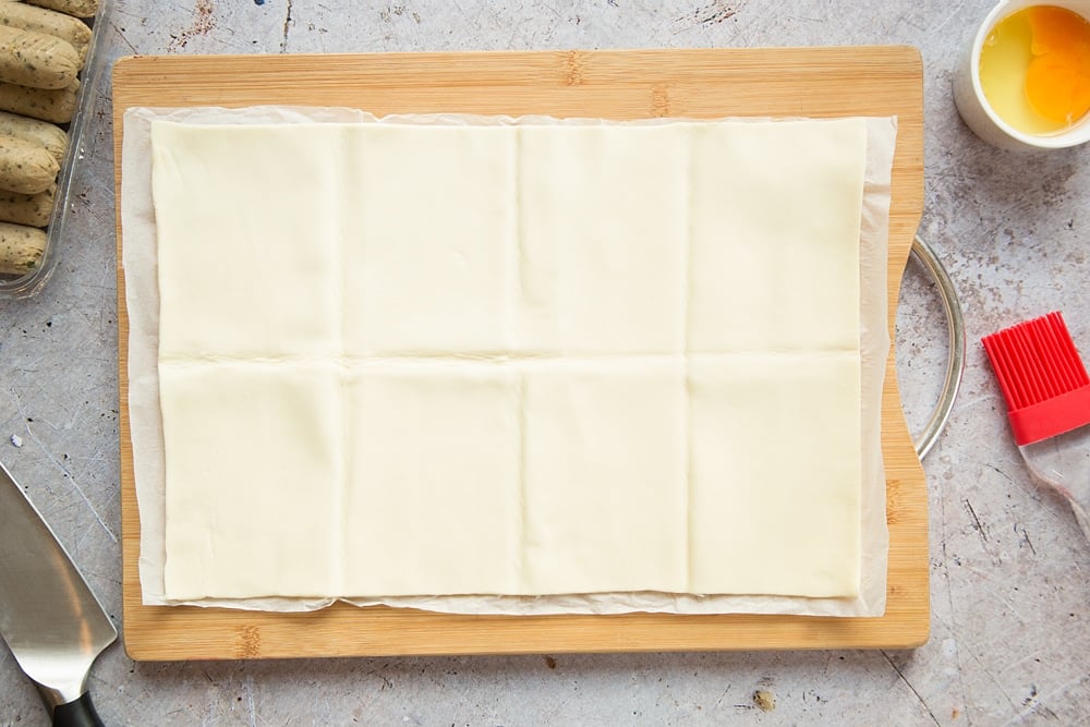 A sheet of puff pastry on a chopping board, folded to give eight sections.