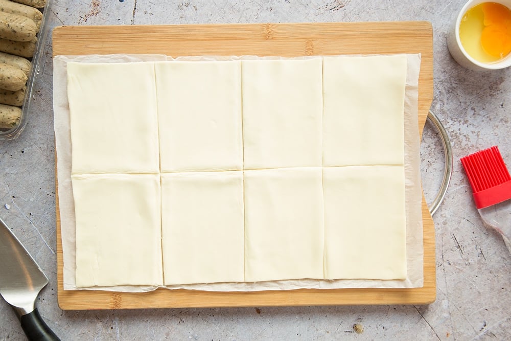 A sheet of puff pastry on a chopping board, cut into 8 pieces.