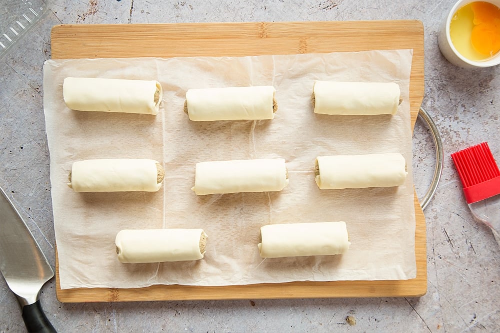 Eight vegetarian sausage rolls on a board, ready to bake.