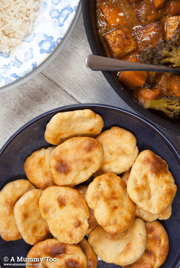 Low fat naan breads in a black bowl with rice and curry in separate dishes.