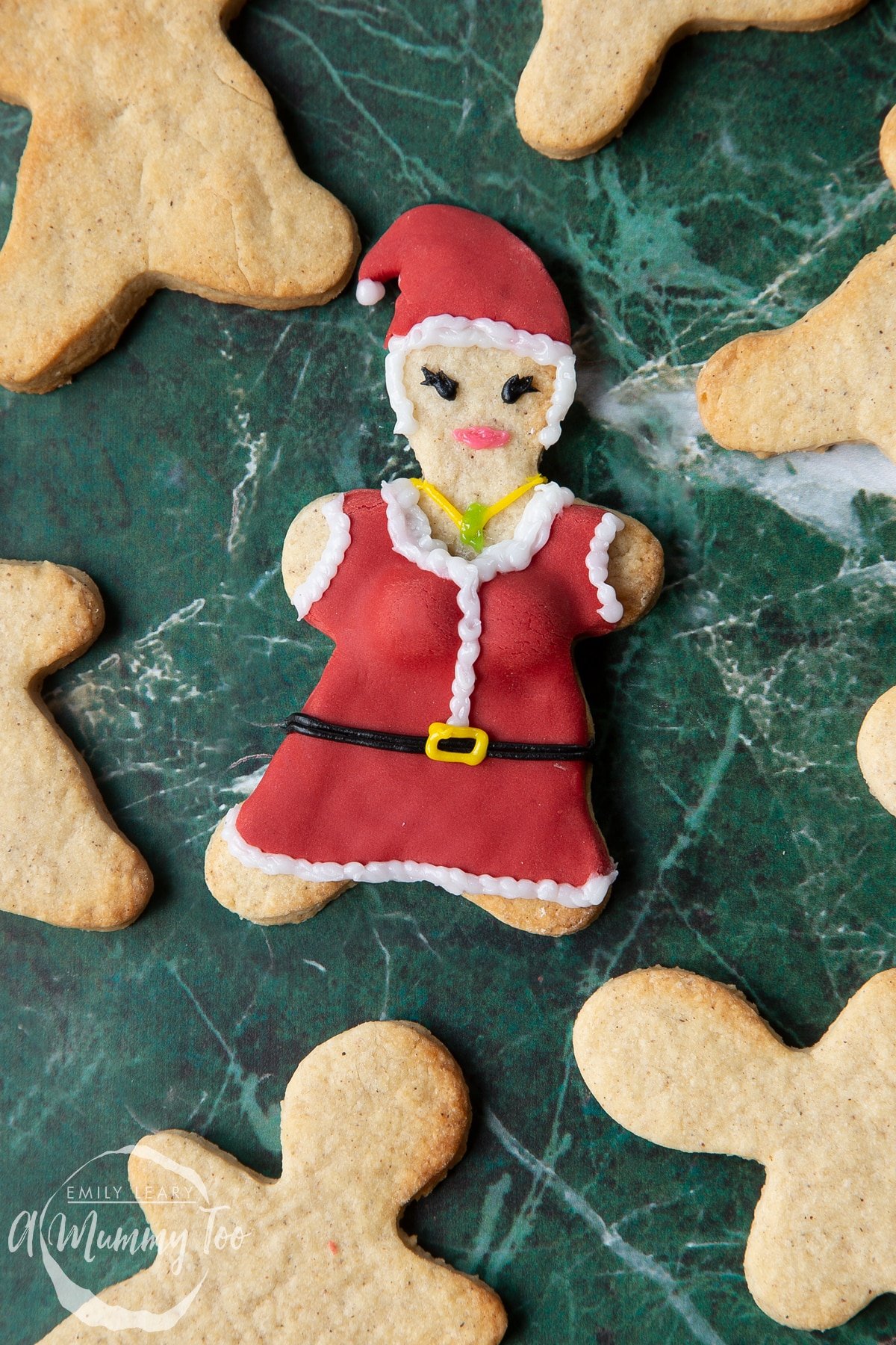 A Mother Christmas cookie, decorated with a suit and hat made from red sugar paste and writing icing.