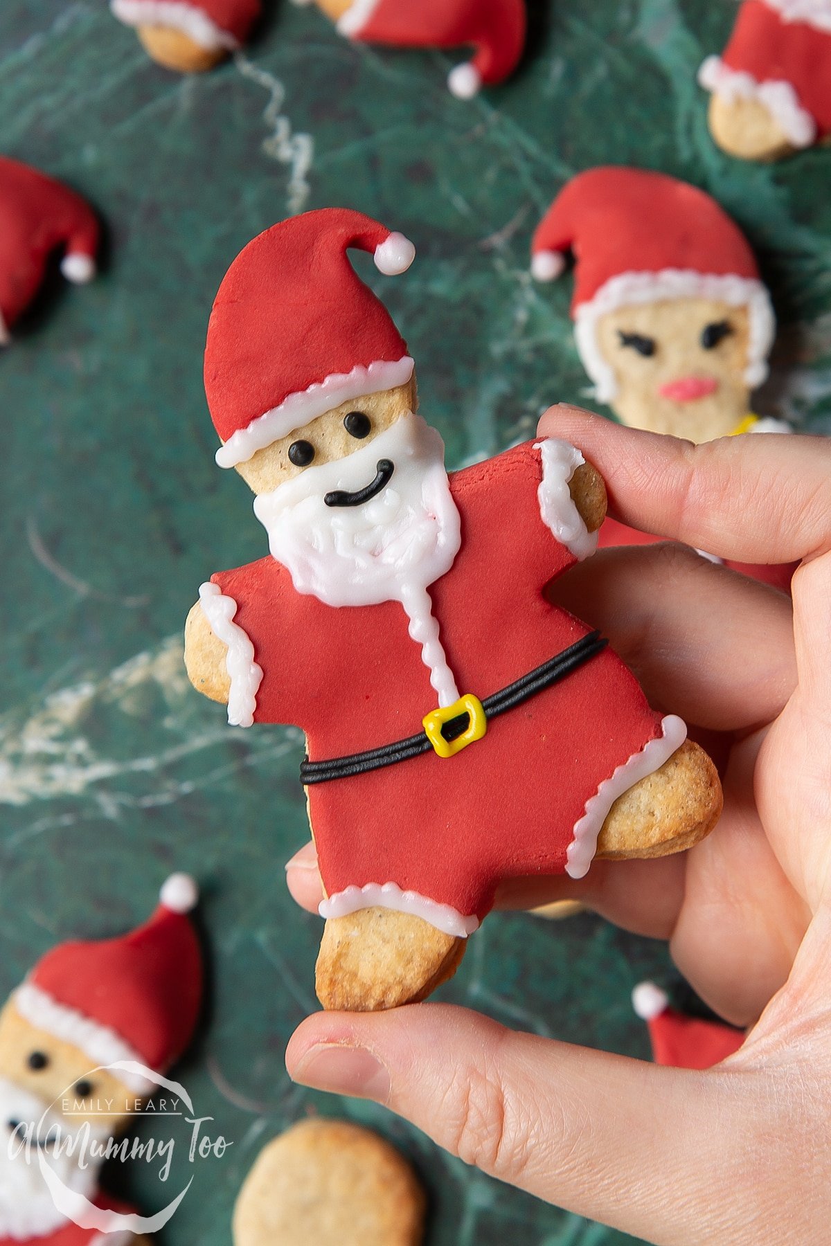 Hand holding a Father Christmas cookie on a green marble surface.