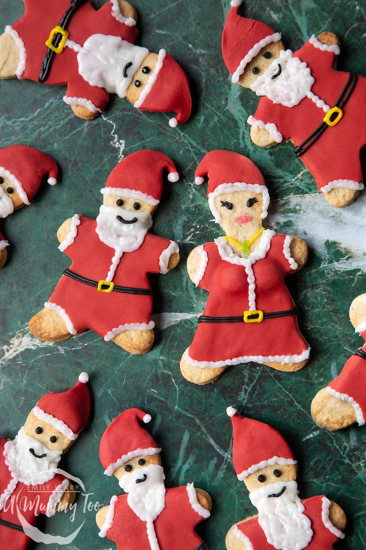 Lots of Father Christmas cookies on a green marble surface. There is also a Mother Christmas cookie.