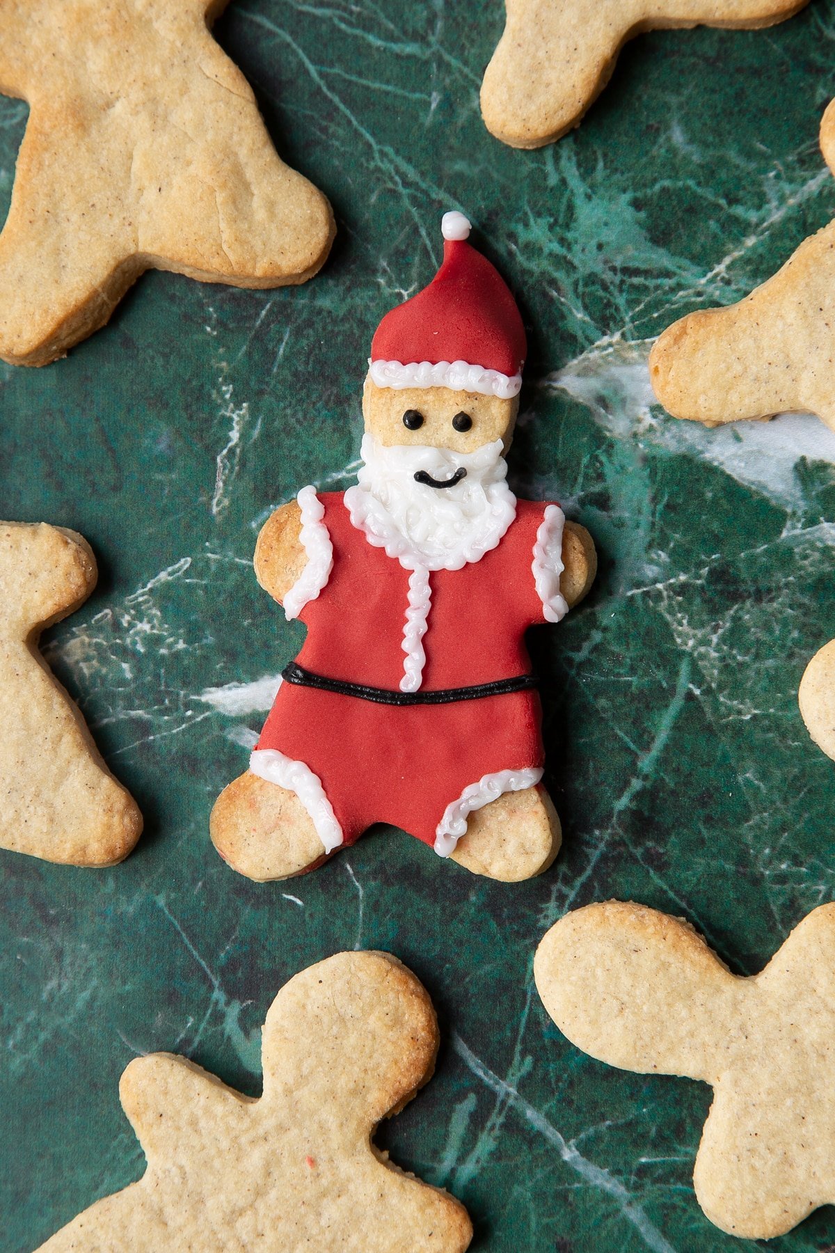 A cookie in the shape of Father Christmas, decorated with a suit and hat made from red sugar paste and writing icing.