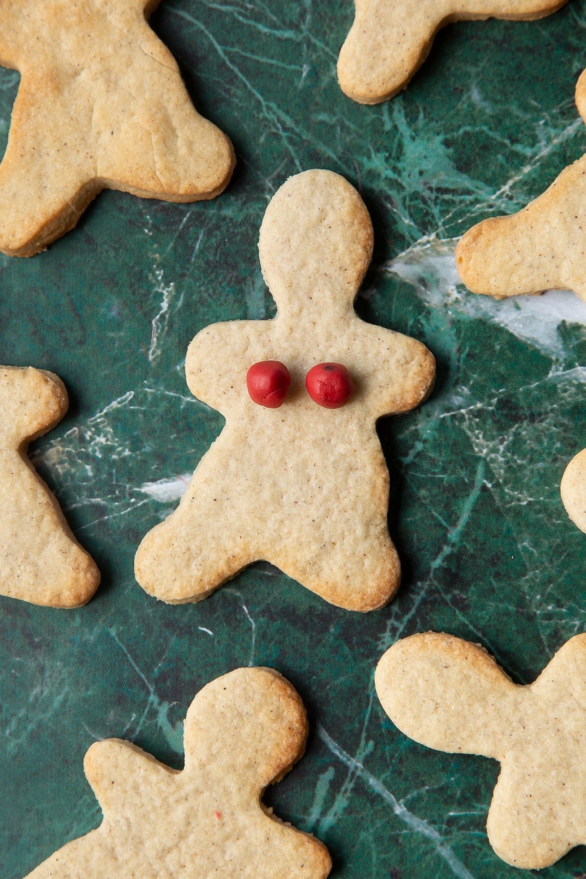 A cookie in the shape of a woman, decorated with two small balls of red sugar paste.