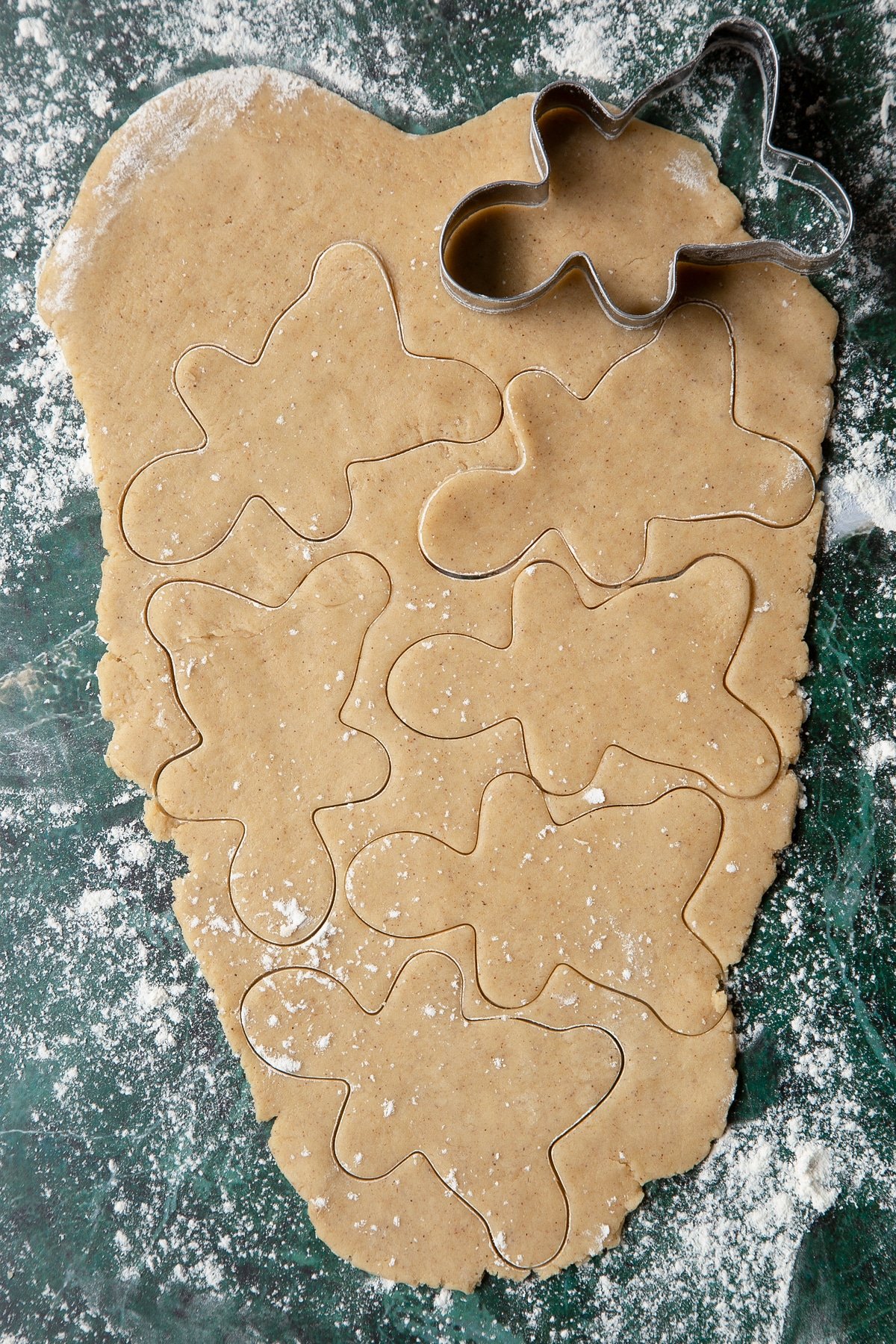Cookie dough rolled out. A gingerbread man cutter has cut several shapes.