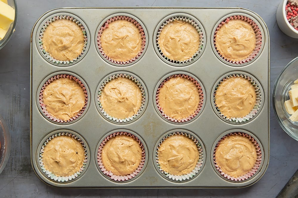 A twelve hole muffin tray lined with muffin cases and the spiced Christmas cupcakes with marzipan frosting cake mixture. 