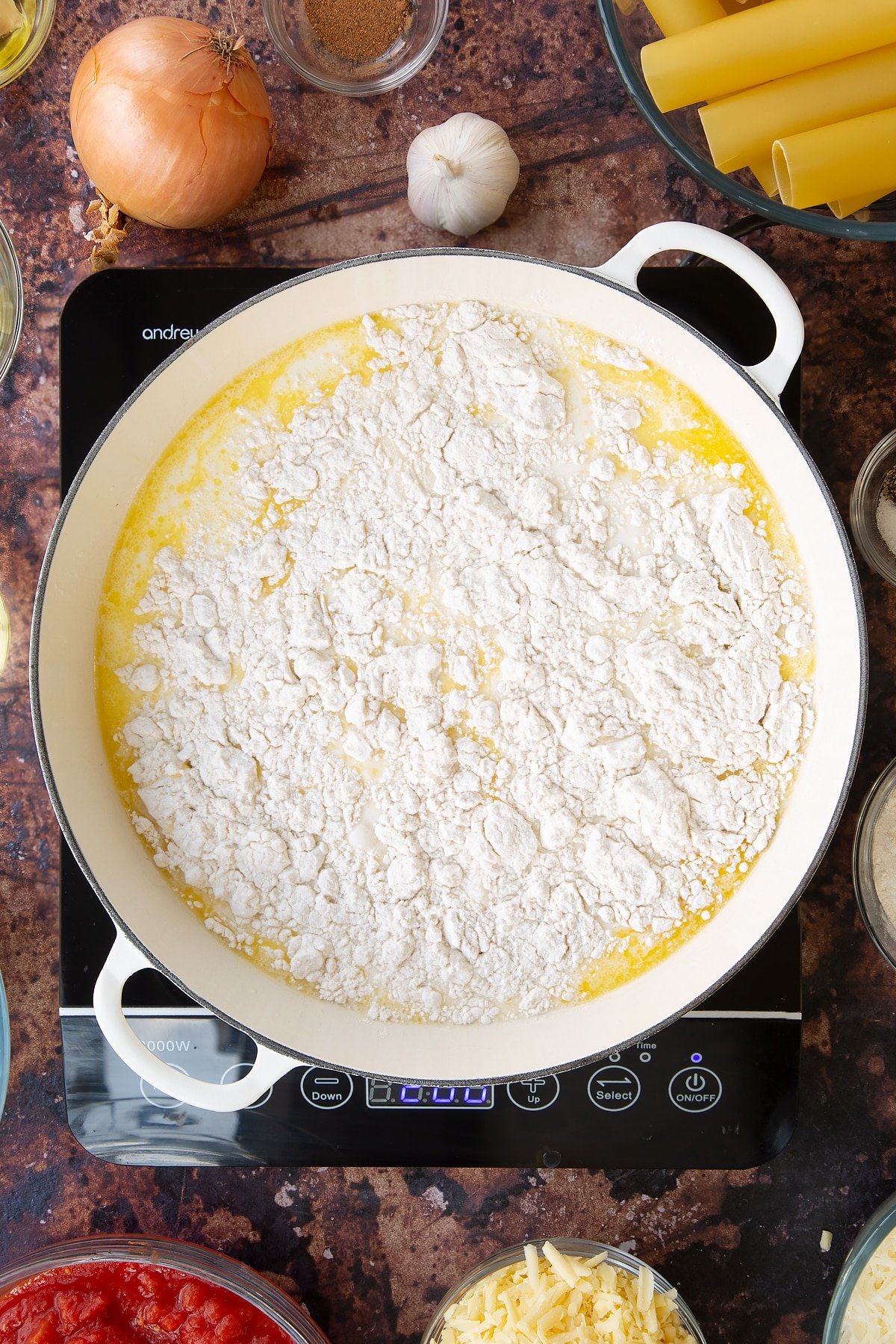 Overhead shot of butter, flour, milk and oil being melted in a pan on top of an induction hob.