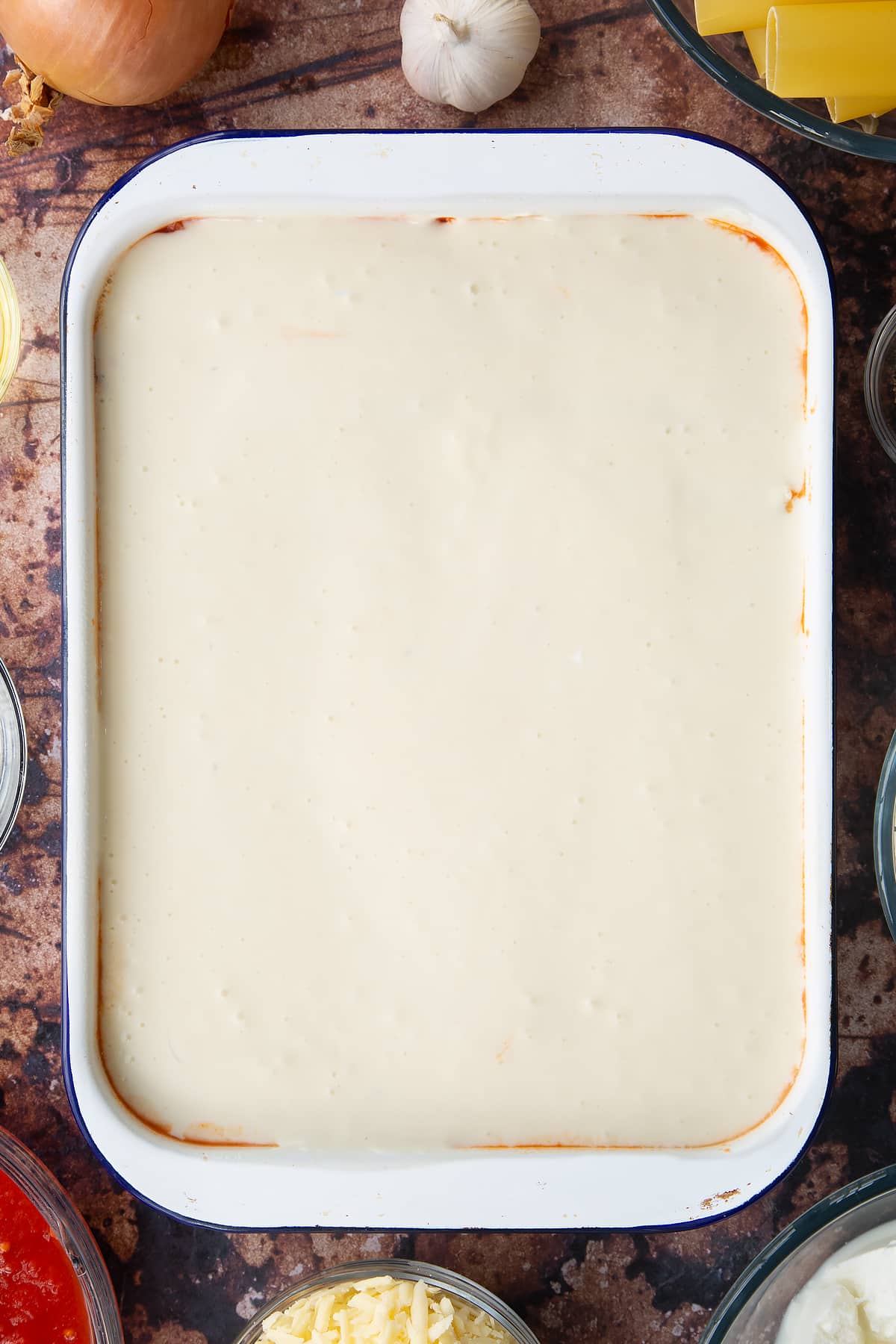 Overhead shot of the white sauce which has topped the spinach and ricotta cannelloni inside of the baking dish.