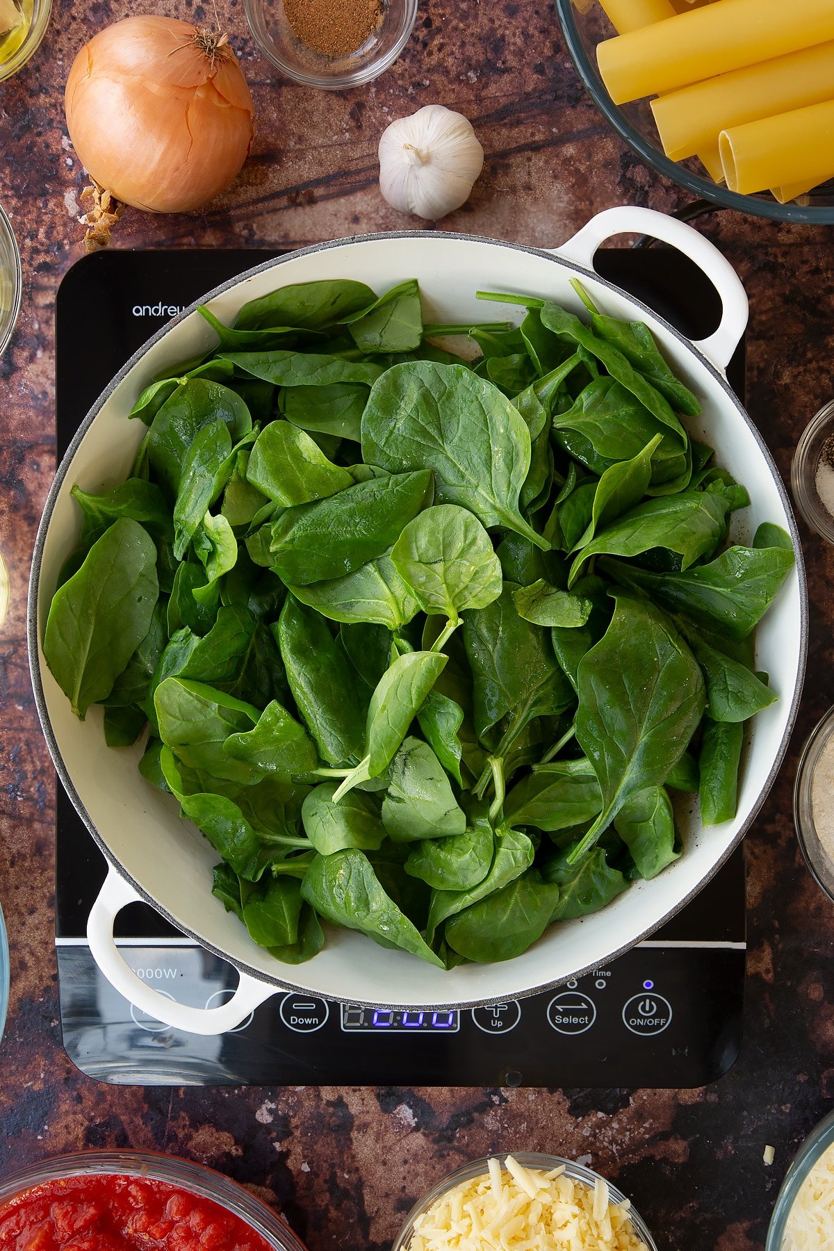 Overhead shot of the spinach inside a pan being cooked on an induction hob.