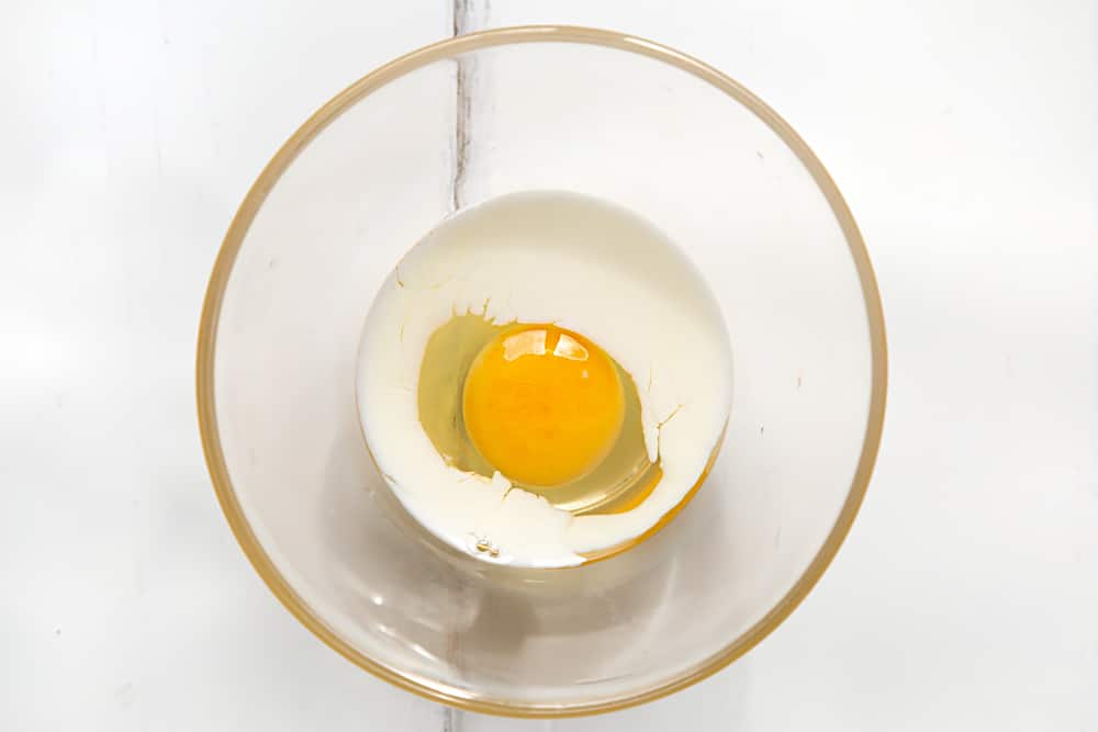 One egg and some milk in a bowl on a white table.
