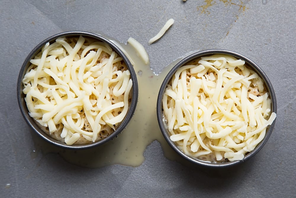 Overhead shot of the two egg rings with crumpets inside covered with milk, egg and cheese.