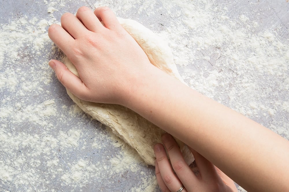 a hand stretching out the flour dough on a floured surface.