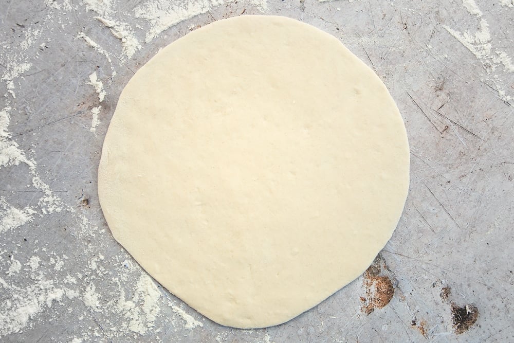 smooth dough flattened out to a large circular dough on a floured surface.