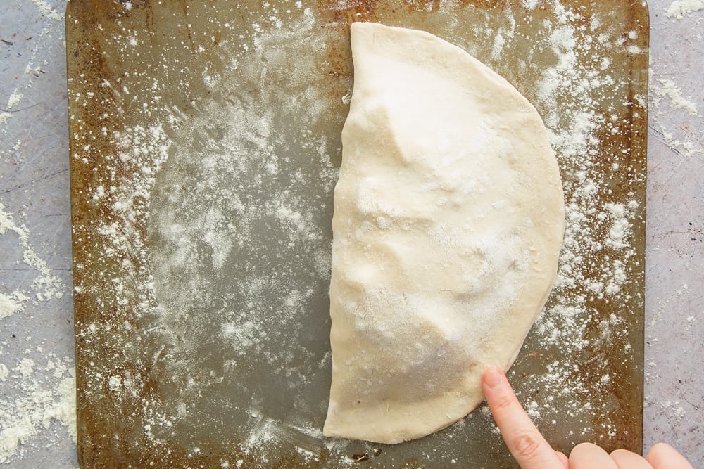 a finger pressing down the edges of  floured dough to create a half circle encasing meat mixture.