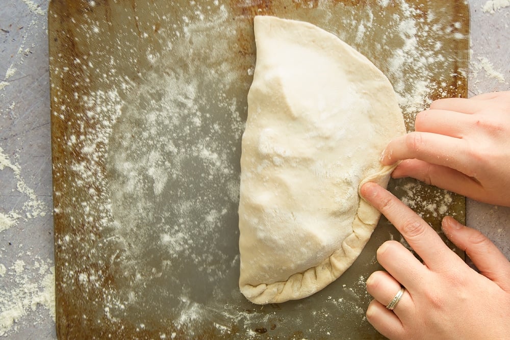 two hands pinching the edges of dough together to create an encased envelope.