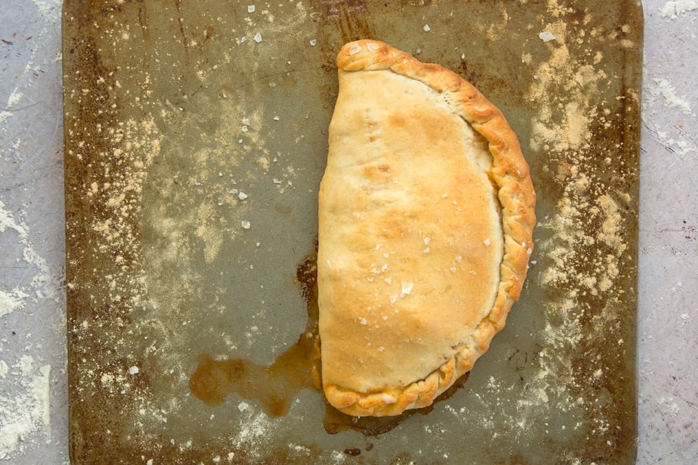 a half circle cooked calzone pizza on a floured baking tray.