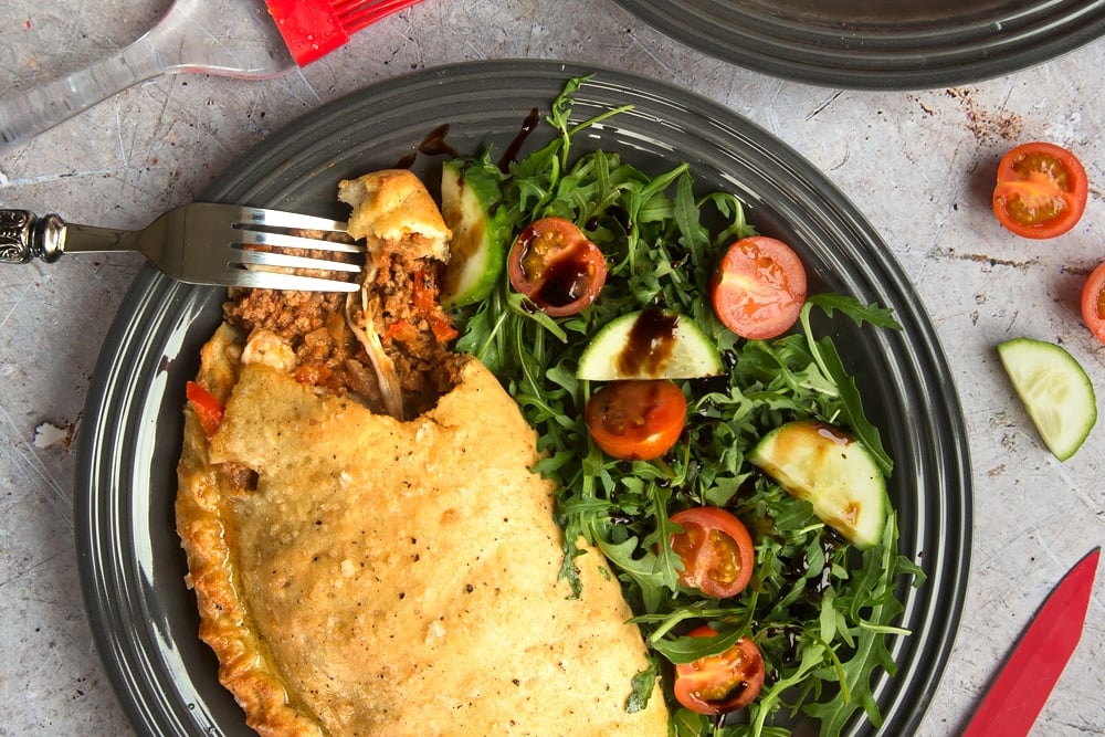 A calzone pizza with a bite missing and a fork on the edge of the plate accompanied by a side salad.
