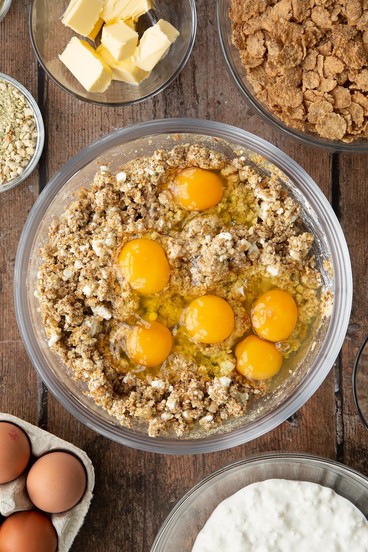 Overhead shot of some of the ingredients required to make the special k loaf together in a clear bowl with six eggs on top prior to mixing in.