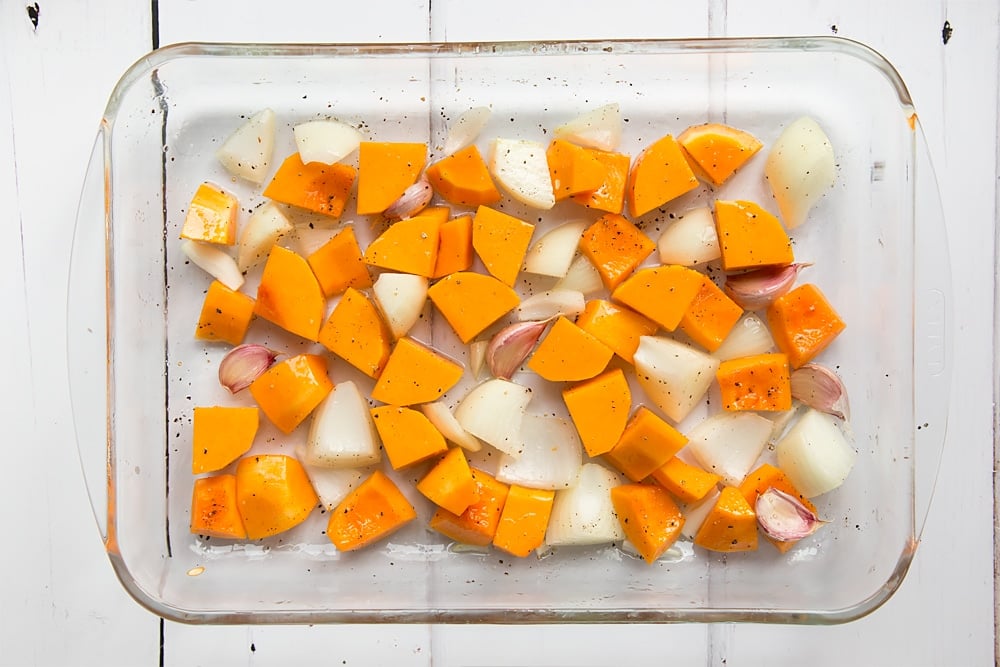Chunks of onion, butternut squash and garlic cloves in a tray ready to make roasted butternut squash soup