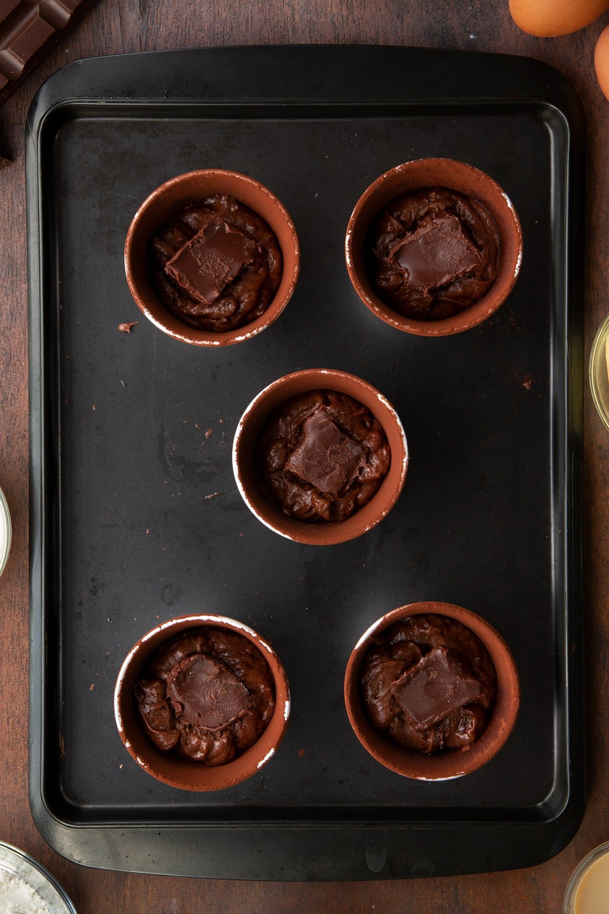 5 ceramic cake moulds filled with chocolate baileys cake mix  topped with a hot chocolate cube on a baking tray.
