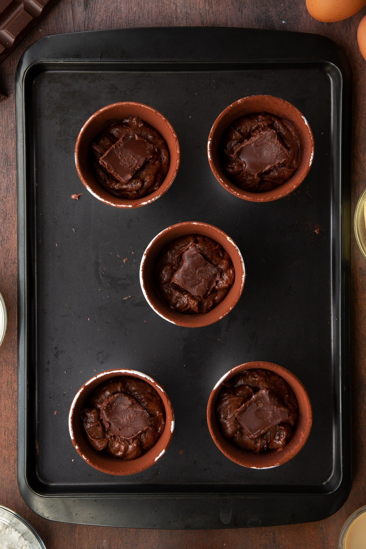 5 ceramic cake moulds filled with chocolate baileys cake mix topped with a hot chocolate cube on a baking tray.