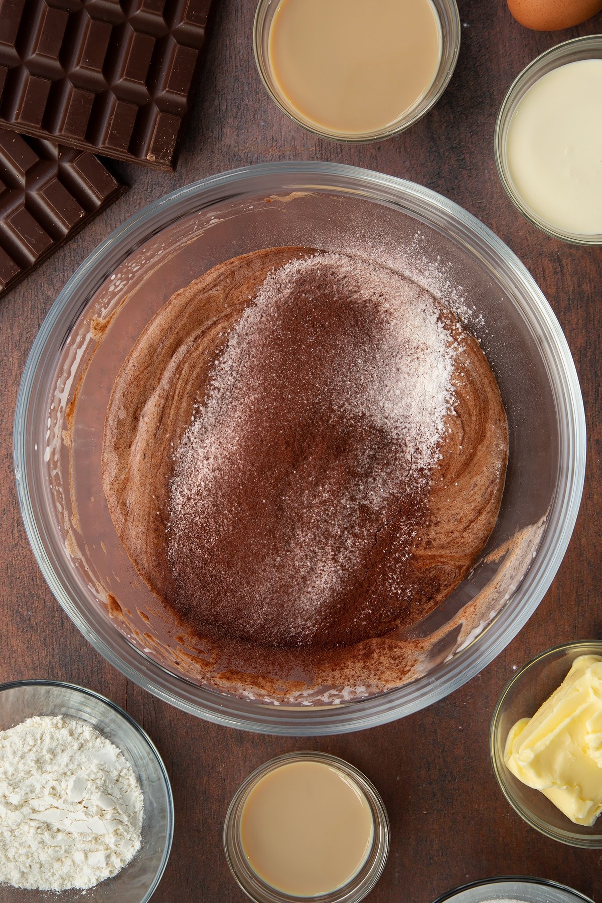 melted chocolate mix topped with flour, cocoa and baking powder in a large clear bowl.