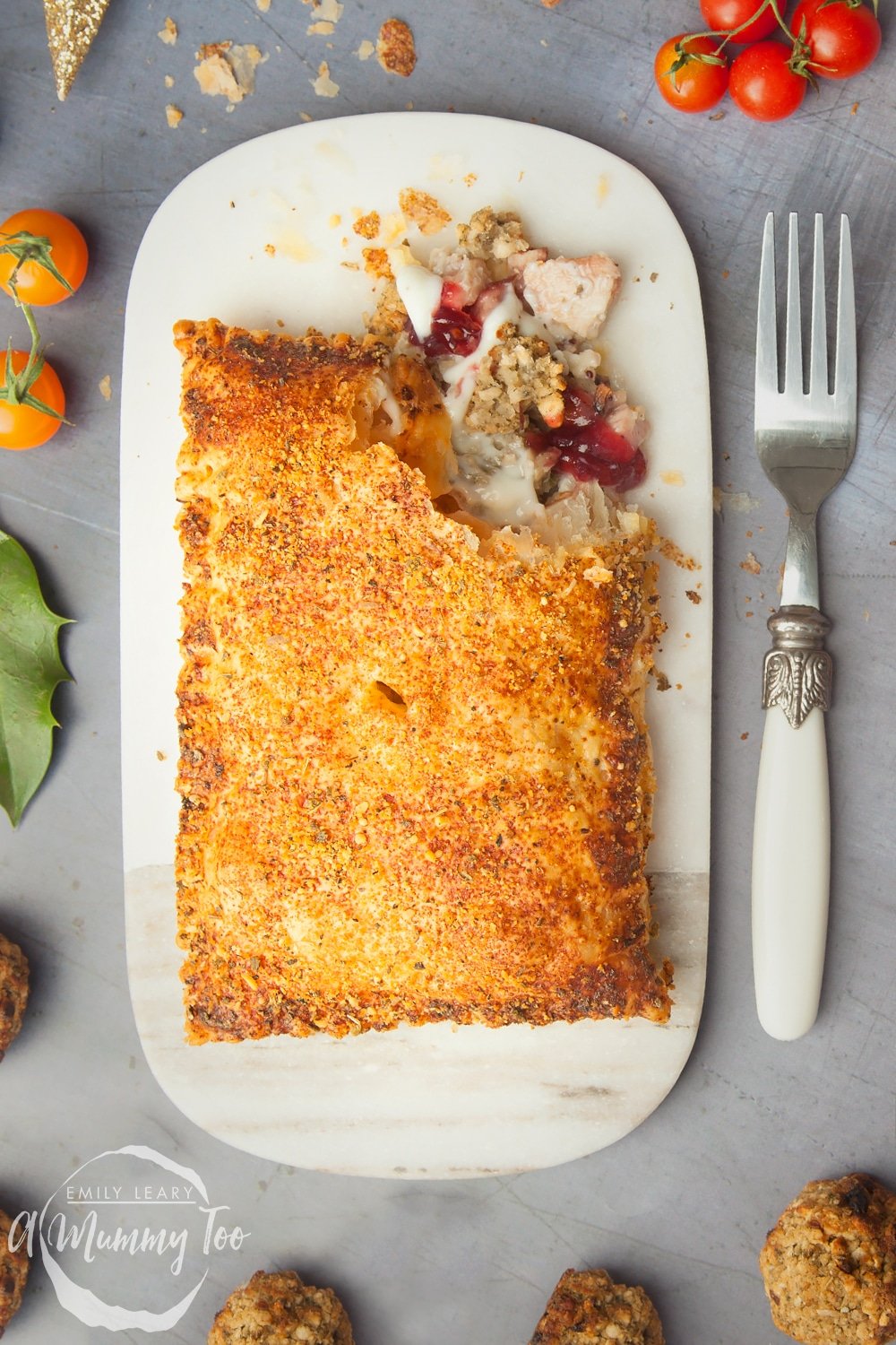 A cut open festive slice on a place with a decorative fork at the side. The background is grey and decorated with different ingredients. 