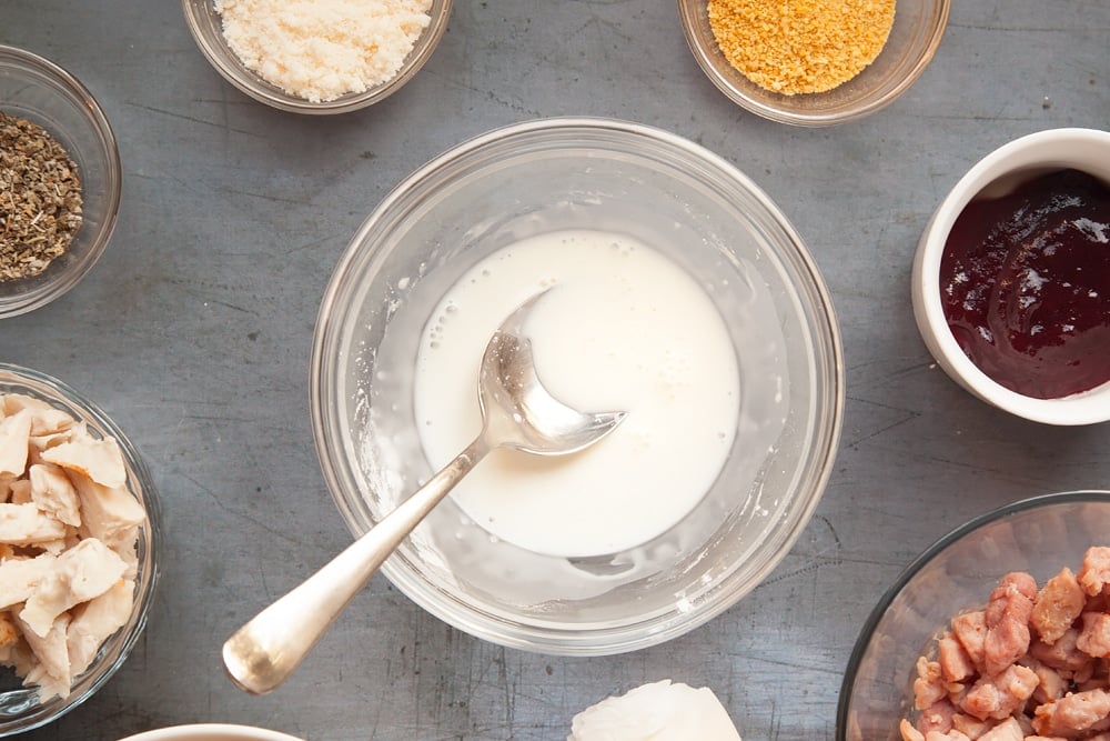 Making white sauce for the festive slice. A spoon is in the bowl with the white sauce ingredients. The other ingredients are in bowls on a grey background. 