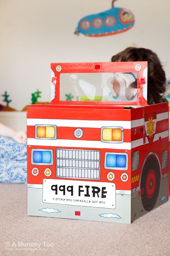 a small child climbing out of their cardboard fire truck